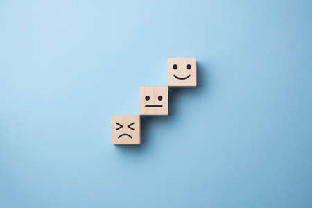 Flipping of wooden cube block from sad to smile emotion on blue background.の写真素材