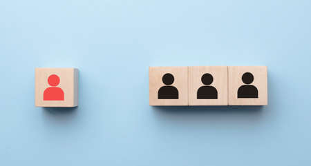 Red wooden cube with person icon stand out from the crowd on blue background. Dissenting opinion,...