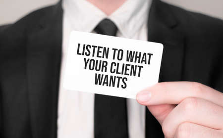 Businessman holding a card with text LISTEN TO WHAT YOUR CLIENT WANTSの写真素材