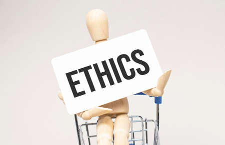 Wooden model of a human in a shopping cart. Gray background. Business, ethics concept, copy space.の写真素材