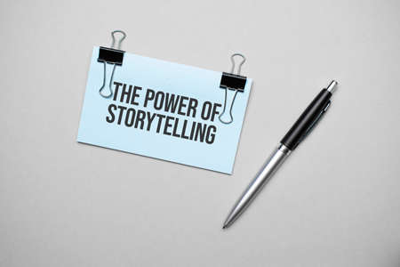 Top view of a business card with text THE POWER OF STORYTELLING, pen, paper clips on a colored background. Business concept.の写真素材