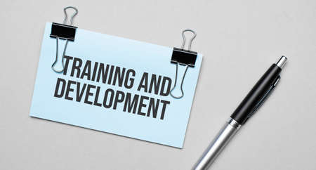 Top view of a business card with text Training and Development, pen, paper clips on a colored background. Business concept.の写真素材