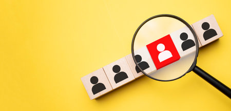 cropped view of woman holding magnifying glass under wooden cubes with logo on yellow backgroundの写真素材