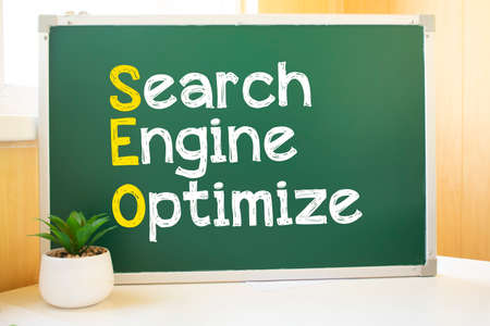 SEO inscription in chalk on the school board, Search engine optimization and websites. Desk, swept balls of paper, computer keyboardの写真素材