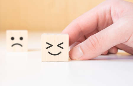 Close up customer hand choose smiley face and blurred sad face icon on wood cube, Service rating, satisfaction concept.の写真素材