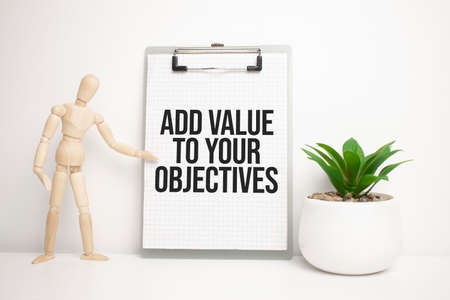 Wooden man shows with a hand to white board with text add value to your objectivesの写真素材