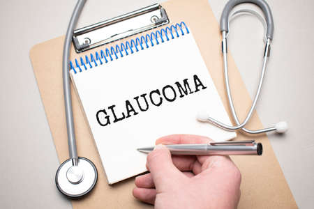 White notepad with the words glaucoma and a stethoscope on a blue background. Medical conceptの写真素材