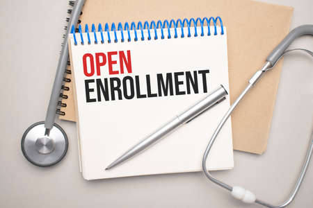White notepad with the words open enrollment and a stethoscope on a blue background. Medical concept