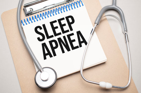 White notepad with the words sleep apnea and a stethoscope on a blue background. Medical conceptの写真素材