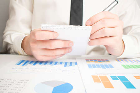 Business analyst working - hand with pen, calculator, coffee, magnifier, worksheet and graphの写真素材