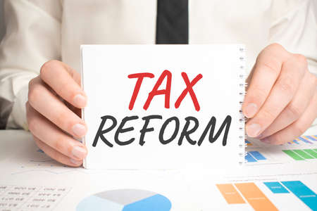 Businessman hold notepad with text TAX REROFM. Financial charts on the desktop. financial and business concept.の写真素材