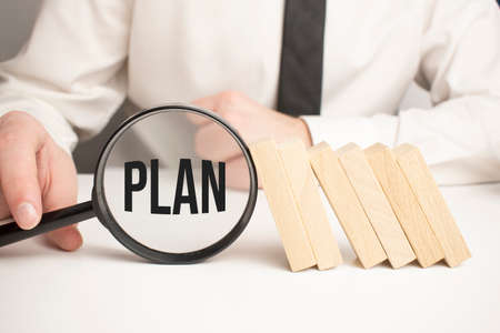 plan text wooden cube blocks and hand holding magnifying glass on table.