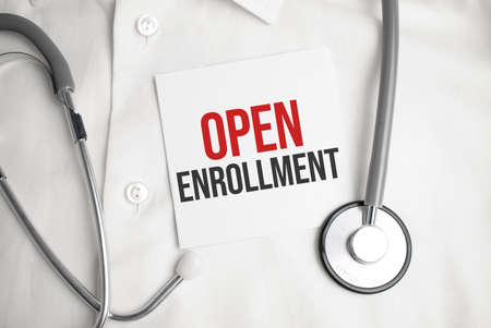 Gray stethoscope and paper plate with a sheet of white paper with text OPEN ENROLLMENT light blue backround. Medical concept.の写真素材