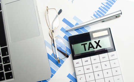 tax text on calculator screen, glasses, laptop and charts. high quality photo
