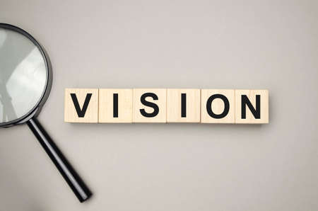 Six wooden blocks lie on a wooden table against the backdrop of a summer garden and create the word VISION. Concept for your designの写真素材