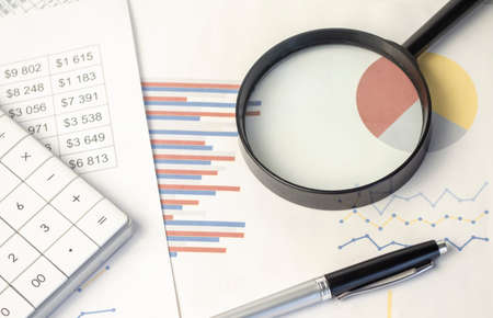 Business graph with magnifying glass and calculator pen on tableの写真素材