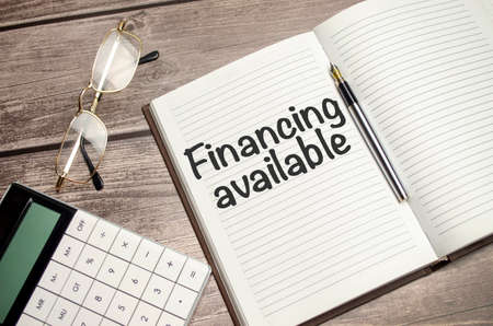 glasses, notepad, pen and pencils on the wood background. business concept. Text FINANCING AVAILABLE