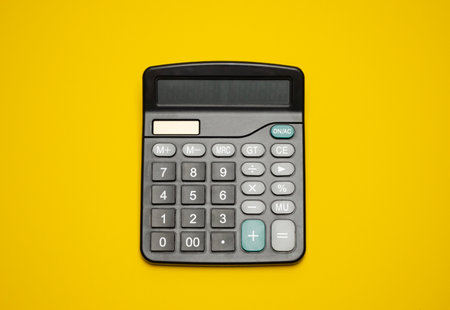 Flat lay or top view of black pen with white calculator on vivid yellow backgroundの写真素材