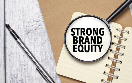 STRONG BRAND EQUITY words on magnifier glass with notebook and penの写真素材