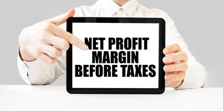 Text NET PROFIT MARGIN BEFORE TAXES on tablet display in businessman hands on the white background. Business conceptの写真素材