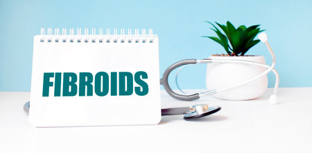 The text FIBROIDS is written on notepad near a stethoscope on a blue background. Medical conceptの写真素材