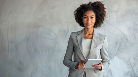 Confident businesswoman with tablet in front of textured gray background. Professional portrait for corporate materials, banner, website.の素材