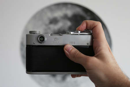 Bucharest Romania - September 2 2020: Male hand holding a FED 3 analog mechanical Soviet Camera, with the image of the Moon in the backgroundのeditorial素材