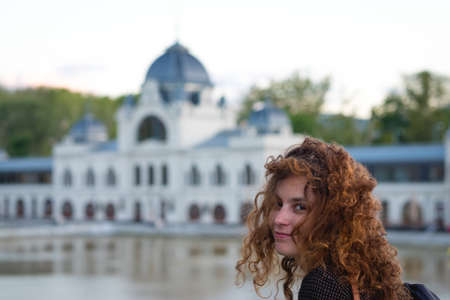 Cute redhead girl looking at the camera smiling with a white baroque building in the background