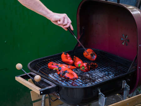 Man hand turning roasted red peppers on a charcoal barbecue fireの写真素材