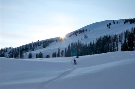 Two people riding up a hill on snowmobilesの写真素材