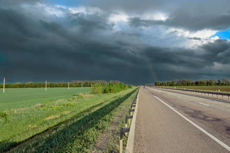 motorway far dark clouds and a rainbowの写真素材