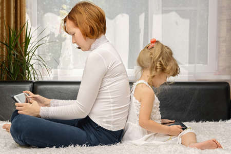 children sitting back to back and looking the tablet