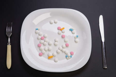vitamin pills lying on a plate and cutlery are nearの写真素材