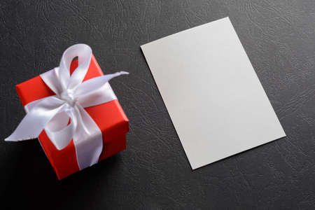 gift red box with a white ribbon tied with a bow next to a sheet of paper for recordsの写真素材