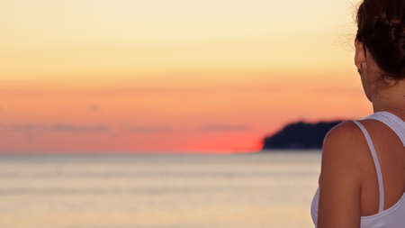 a girl at sunset by the sea looks into the distance of a beautiful sunset rests and enjoys the tourist seasonの写真素材