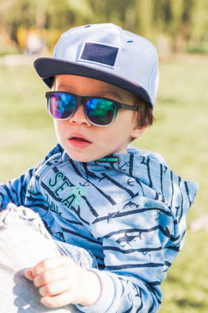 Child blonde 3-4 years in blue with hat and sunglasses held by momの写真素材