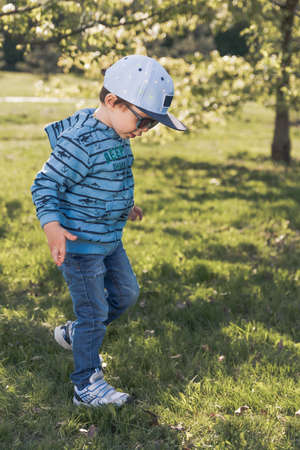 Child blond 3-4 years in blue with hat and sunglasess running around the Parkの写真素材