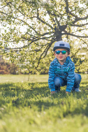 Child blonde 3-4 years in blue with hat and sunglasses running around the parkの写真素材