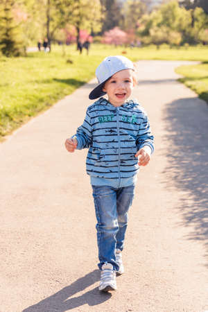 Child blonde 3-4 years in blue with hat and sunglasses running around the park at sunsetの写真素材