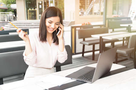 Young pretty woman speaking on mobile phone and sitting in cafe with notebook.の写真素材