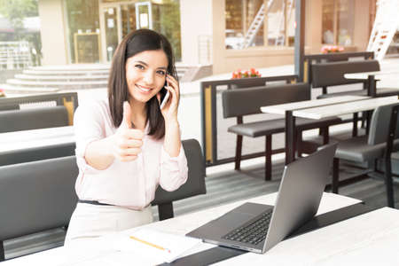 Young business woman sitting at table in cafe, talking on cellphone. Freelancer working online.の写真素材