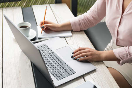Close up portrait of a young woman working on laptop and writing, coffee on the table.の写真素材