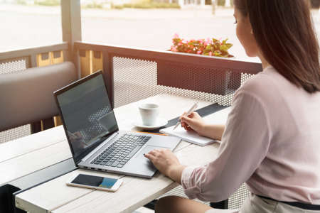 Close up portrait of a young woman working on laptop and writing, coffee on the table.の写真素材