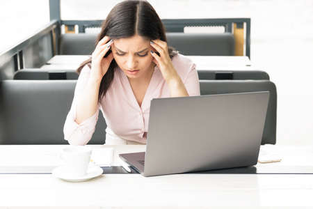 A tired woman holding her head in front of her laptop, having headache and being exhausted of work.の写真素材