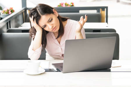 A tired woman holding her head in front of her laptop, having headache and being exhausted of work.の写真素材