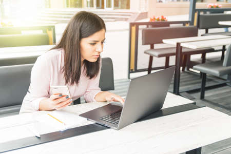 Focused young woman working in office, sitting at desk, using laptop, holding the phoneの写真素材