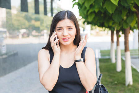Portrait of a shocked young girl speaking on the phone in parkの写真素材