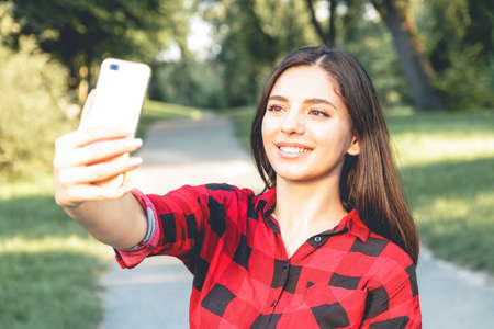 Portrait of a beautiful brunette girl in a red, plaid shirt, taking selfie, video chatting.のeditorial素材