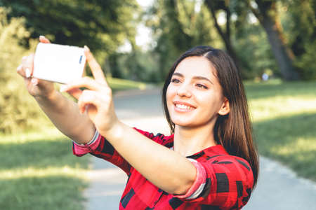 Portrait of a beautiful brunette girl in a red, plaid shirt, taking selfie, video chatting.のeditorial素材