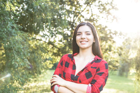 Smiling beautiful brunette girl in a red, plaid shirt, with arms crossed.のeditorial素材